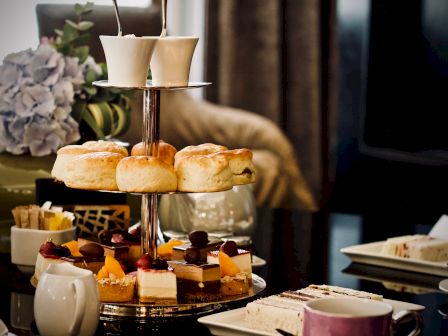 A tiered tray with scones and assorted cakes, flanked by teacups and a teapot, set up for a cozy afternoon tea gathering.