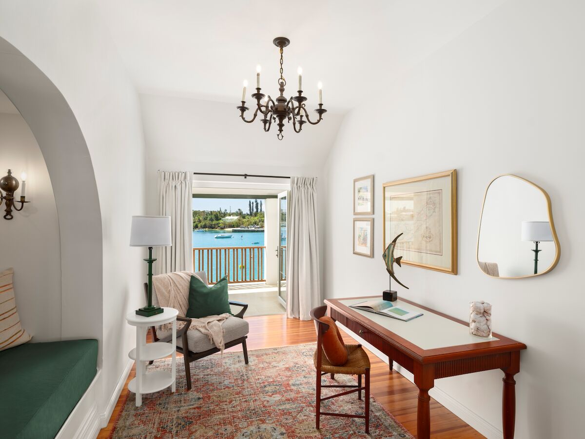 Bright living room with a chandelier, lamps, framed art, a console table, and open doors to a scenic waterfront view.