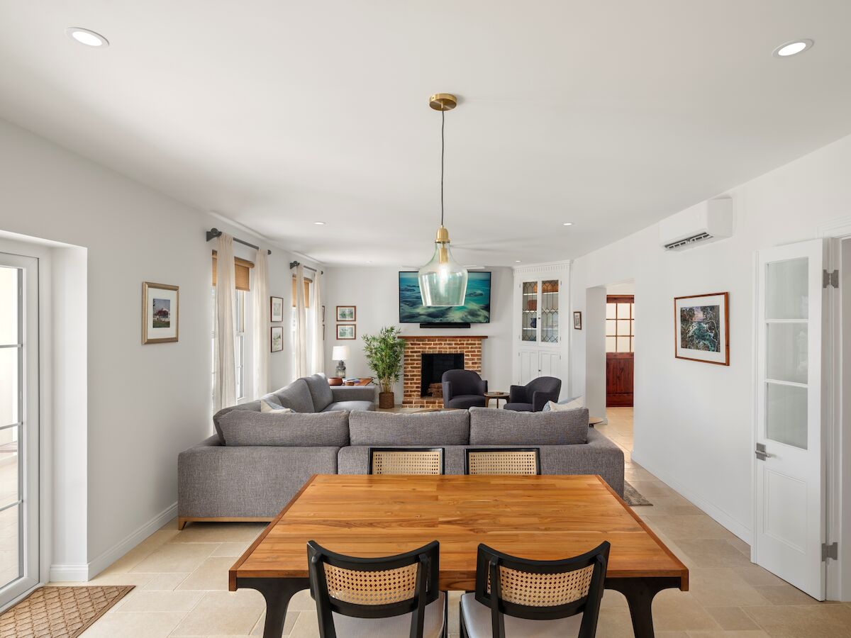 Bright living room with gray sectional sofa, brick fireplace, wall TV, pendant lamp, framed art, curtains, and windows.