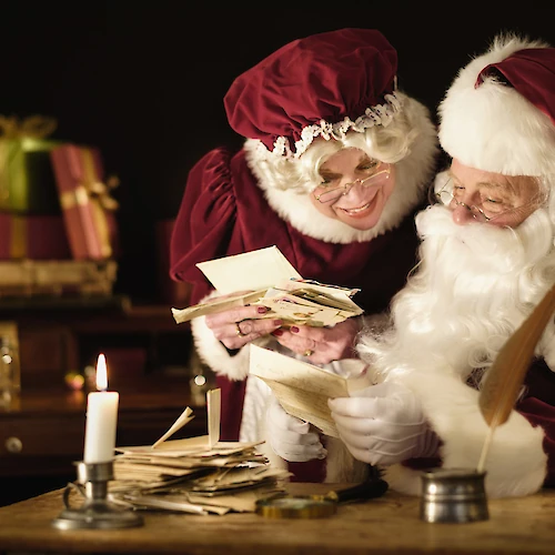 Two Santa figures counting money/cards by candlelight, with gifts in the background&mdash;a cozy, festive scene of holiday cheer and exchange.