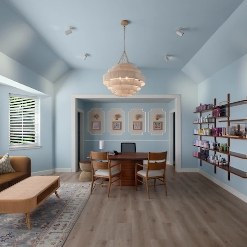 Bright living room with a dining table under a chandelier, couch and rug, plus a wall of shelves with candles and books.