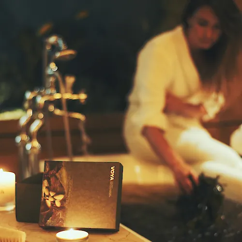 A candlelit table with a &ldquo;vova&rdquo; book/card box in the foreground, while two people sit blurred in the background.