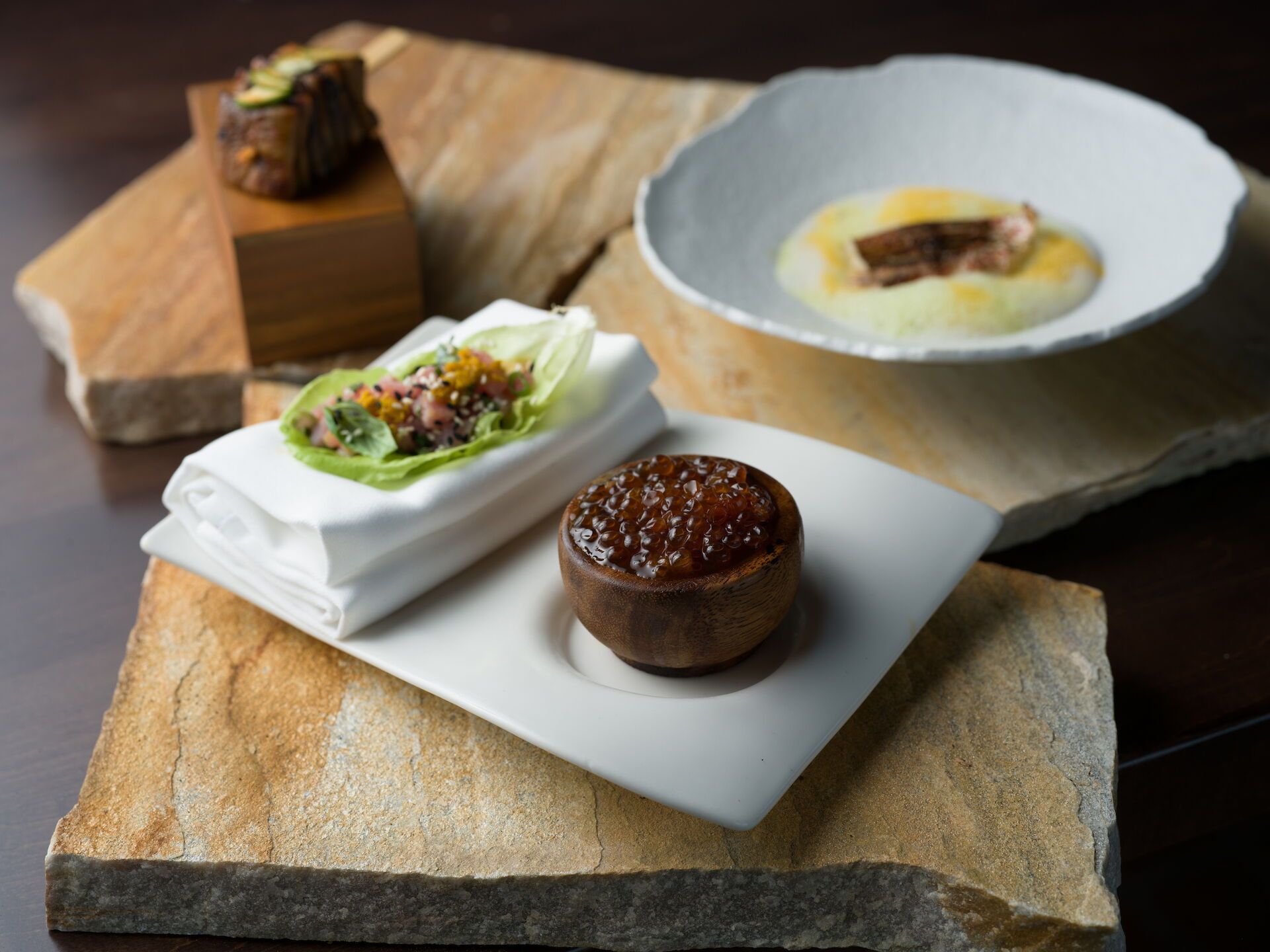 An appetizer spread with lettuce wraps, a small meat sandwich, a bread bowl with sauce, and a dessert cup.