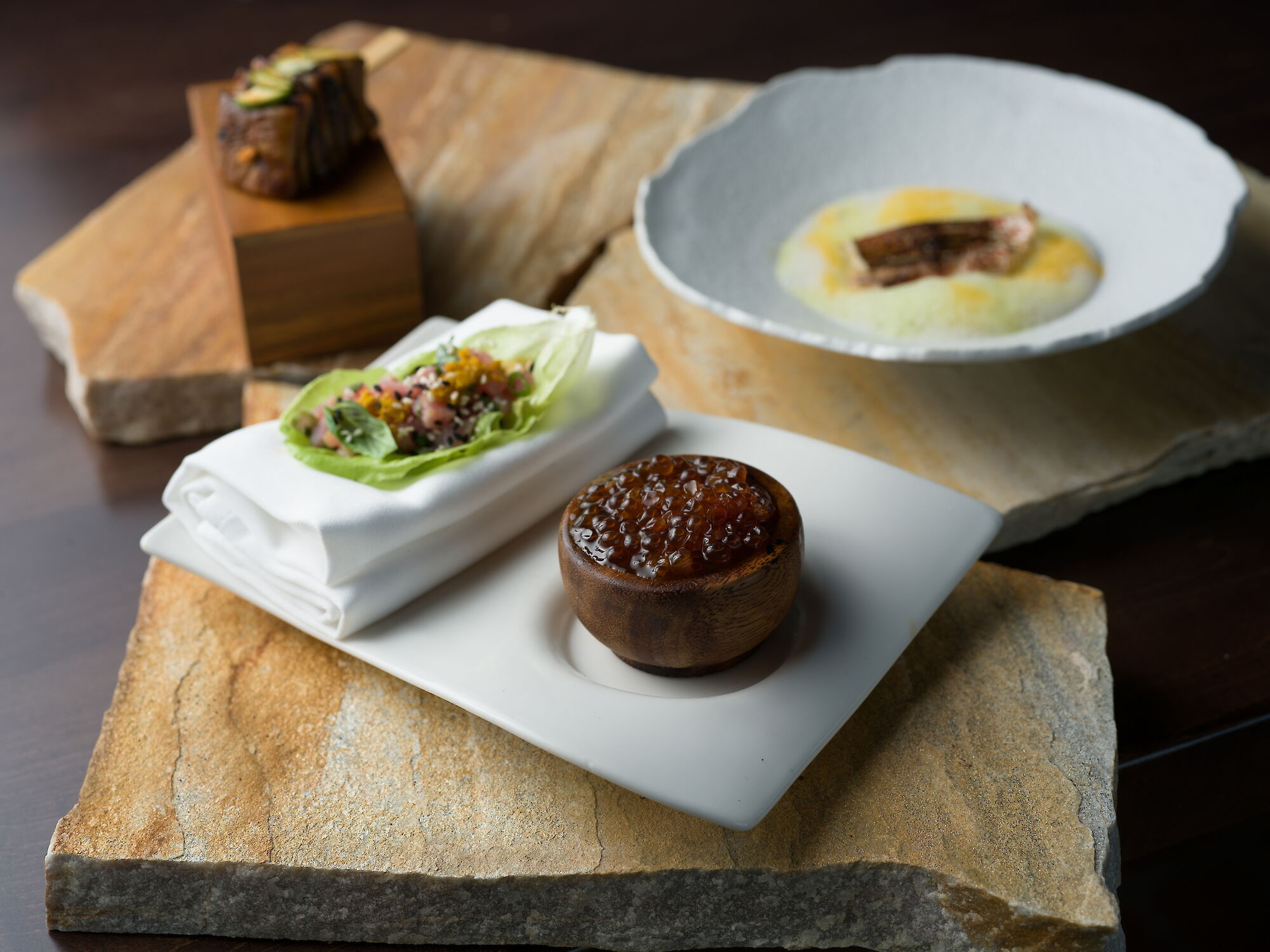 An appetizer spread with lettuce wraps, a small meat sandwich, a bread bowl with sauce, and a dessert cup.