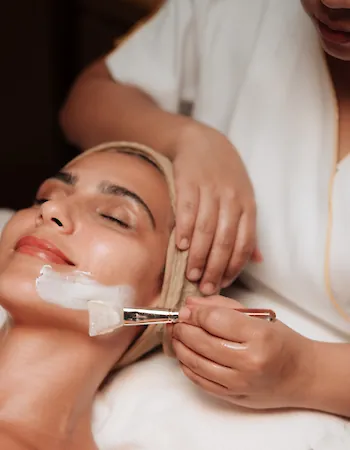 Guest enjoying a relaxing facial treatment as a spa therapist applies a skincare mask.