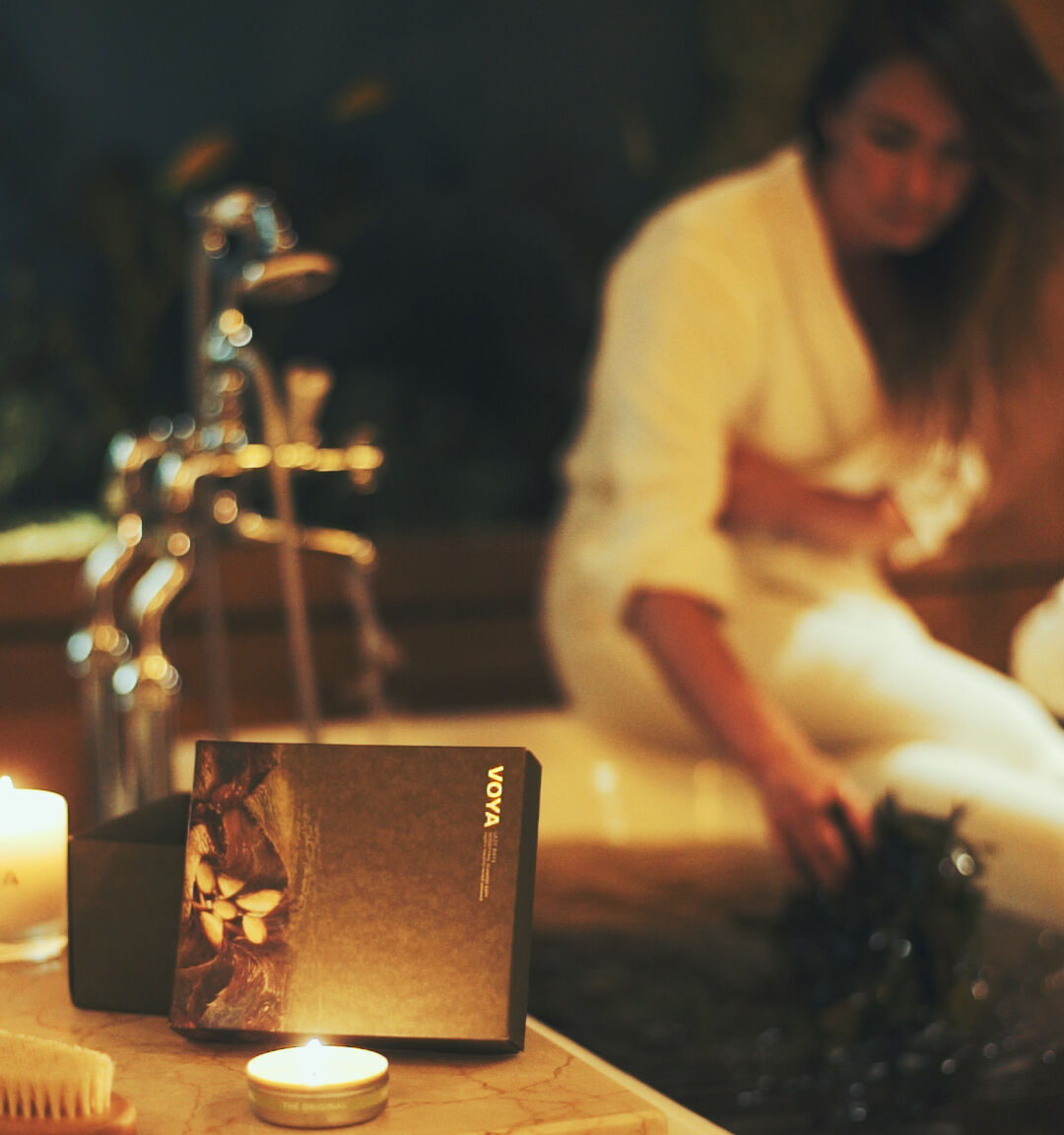 A candlelit table with a &ldquo;vova&rdquo; book/card box in the foreground, while two people sit blurred in the background.