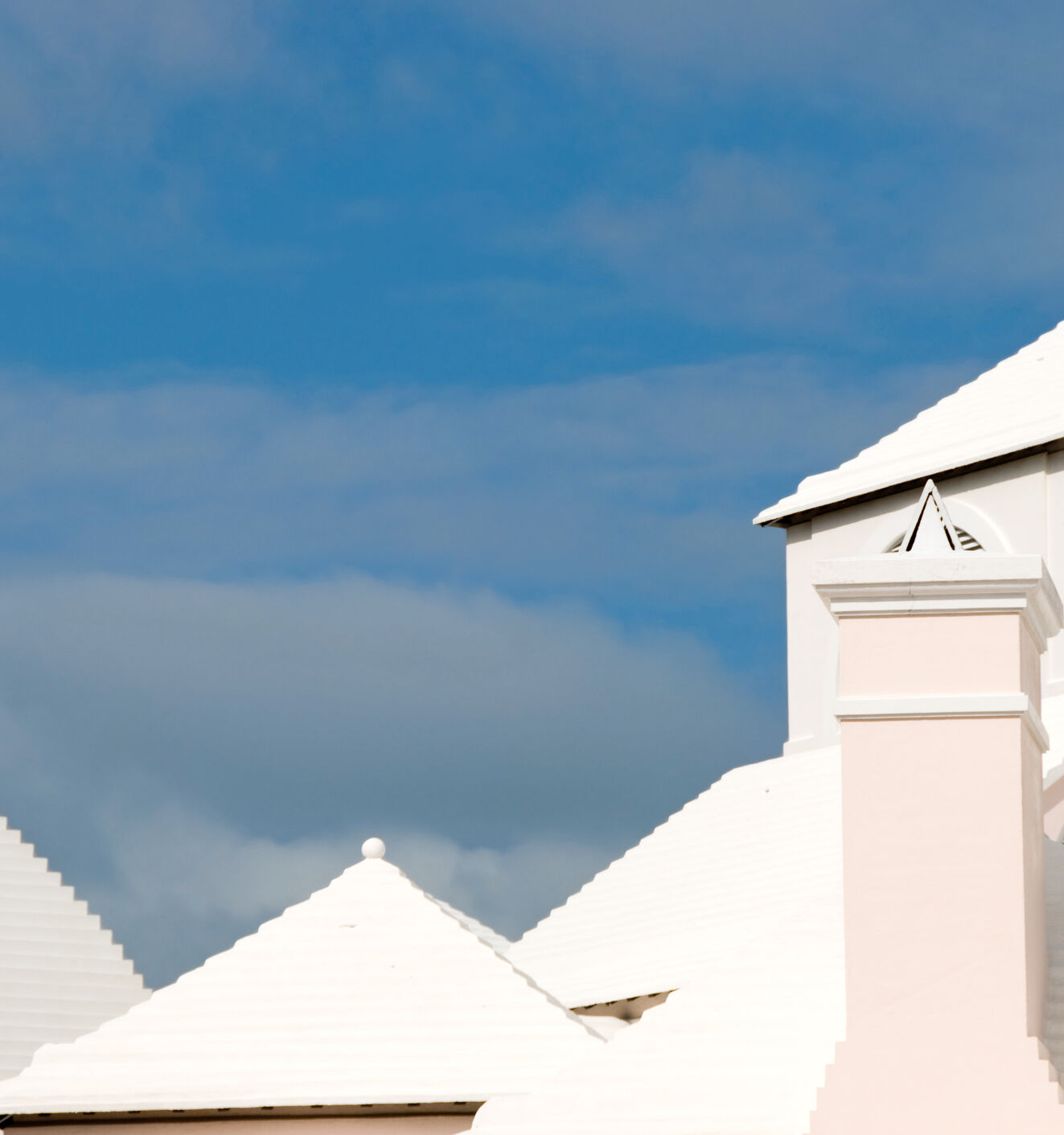 A white church-like building with arched vents and domes rises against a clear blue sky with scattered clouds.
