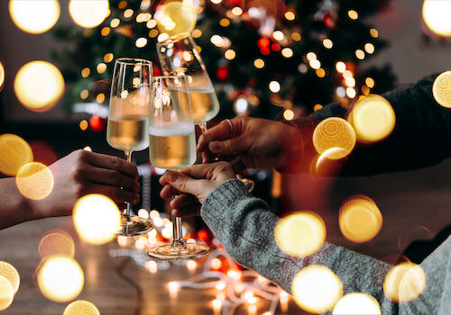 People clinking champagne flutes in a festive celebration with warm bokeh lights in the background.