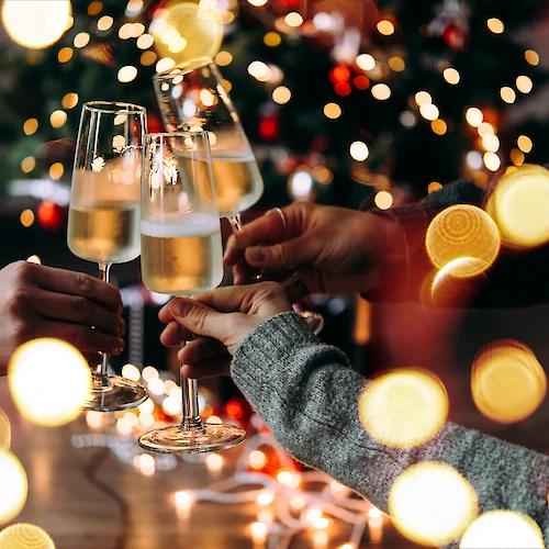People clinking champagne flutes in a festive celebration with warm bokeh lights in the background.