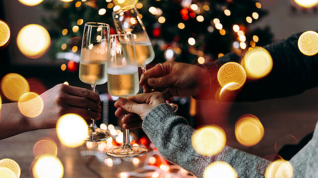People clinking champagne flutes in a festive celebration with warm bokeh lights in the background.