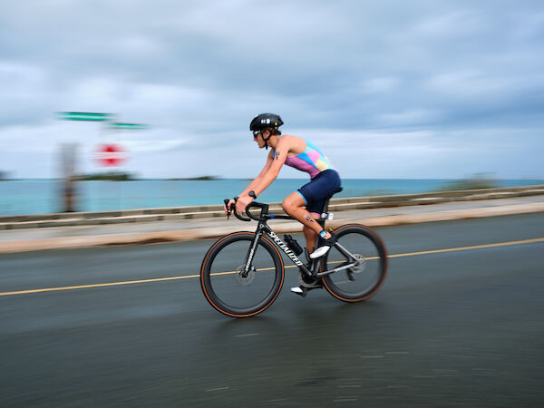 A cyclist riding a road bike on a seaside highway, blurred background from motion, overcast sky, ocean in the distance, on a coastal route.