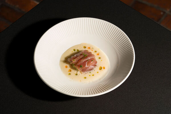 A dish with sliced raw fish on a white sauce, garnished with herbs and small orange bits, presented in a white bowl.