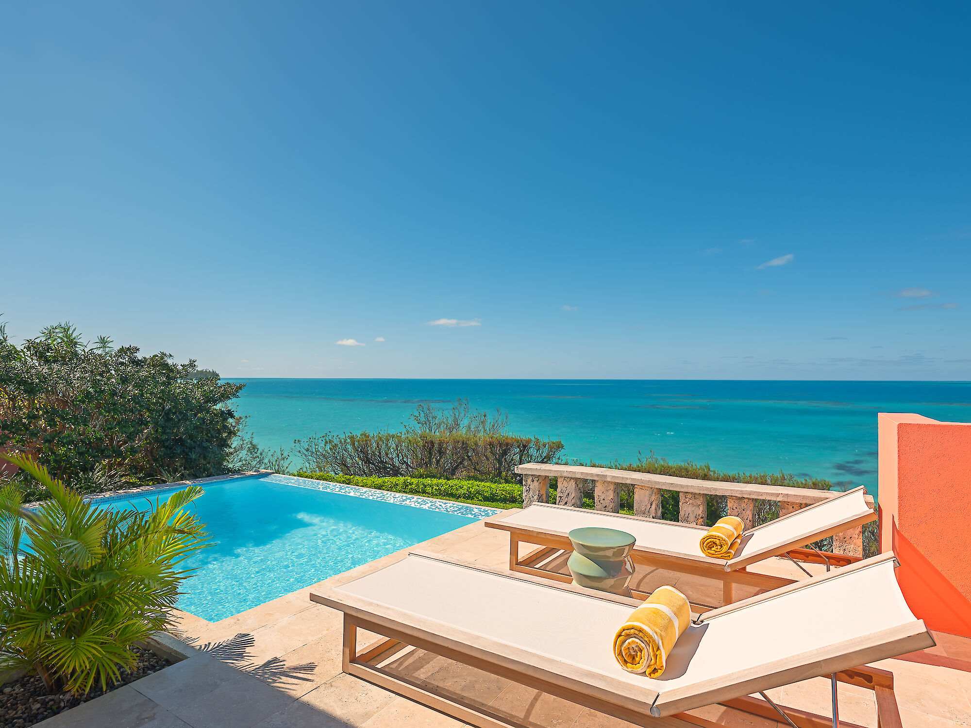 Ocean view from a poolside patio with loungers and towels.