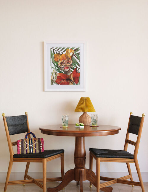 A small round table with two chairs, a lamp, glasses, and a painting above it on the wall, creating a cozy setup.