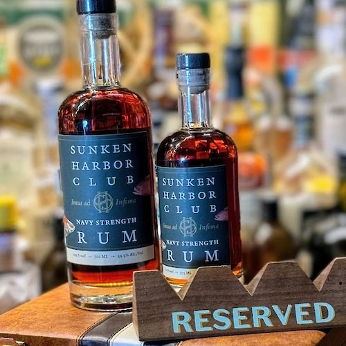 Two bottles of Sunken Harbor Club Rum are on display, placed on a wooden tray with a "RESERVED" sign in a bar setting.