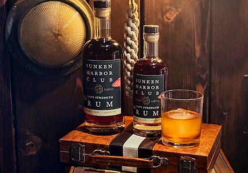 Two bottles of rum, a glass with ice, a bell, and a wooden decor setup on display.