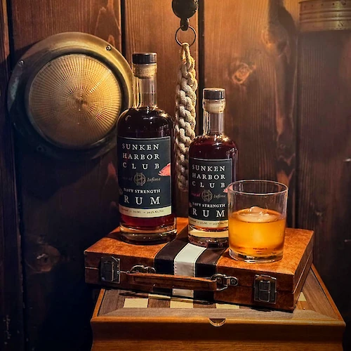 Two bottles of rum, a glass with ice, a bell, and a wooden decor setup on display.