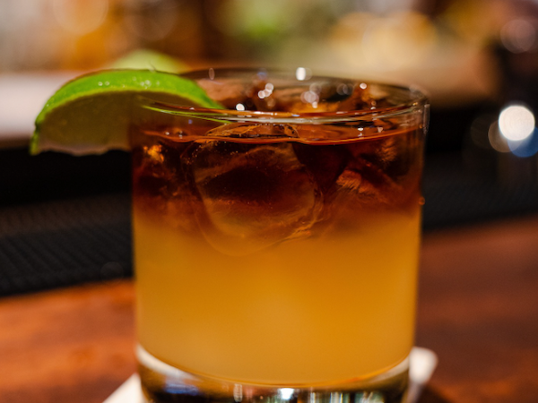 A cocktail in a glass with a lime wedge and ice sits on a napkin at a bar.