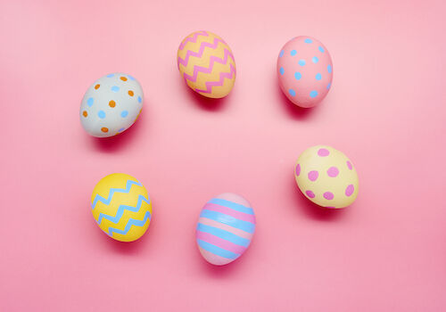 The image shows six colorful Easter eggs with various patterns on a pink background.