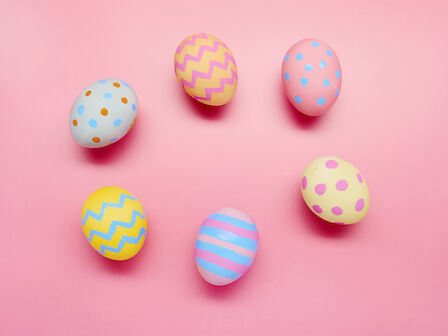 Six colorful eggs with different patterns, like dots and stripes, on a pink background.