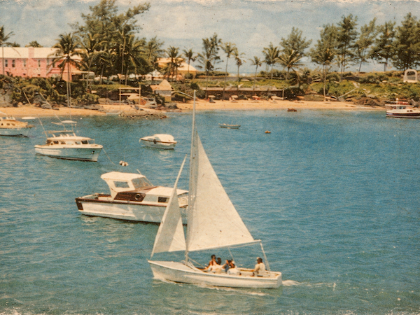 Colorful coastal scene: a small sailboat glides near shore with people aboard, palm trees lining a sunny beach, other boats anchored nearby.