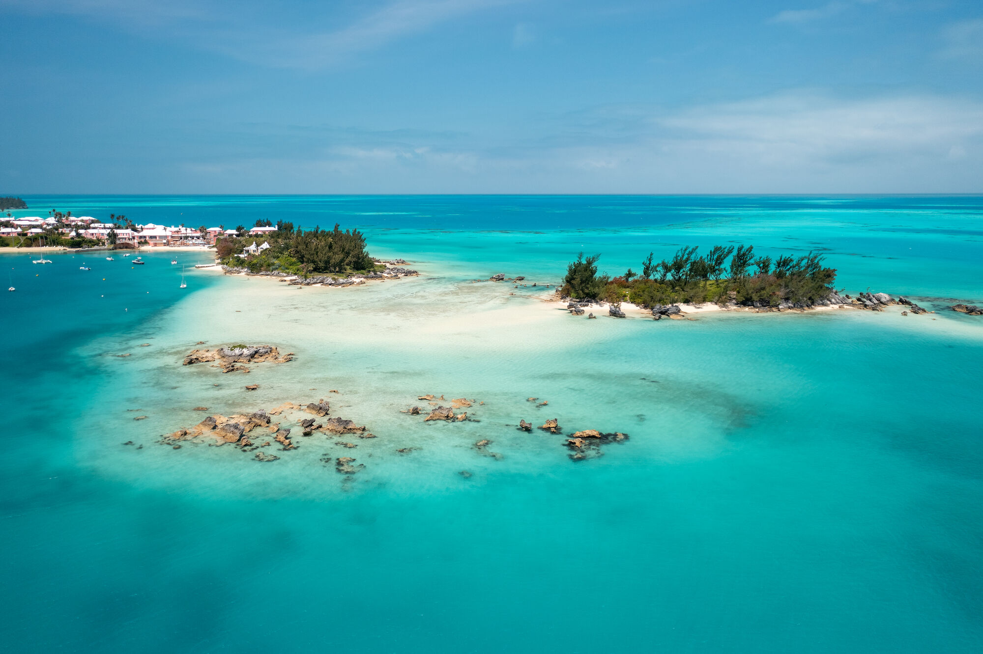 A tropical island with white sandy beaches and turquoise waters, surrounded by lush greenery under a clear blue sky.