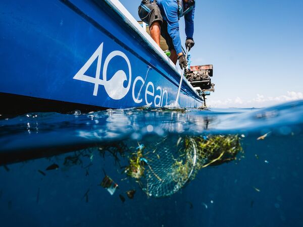 The image shows a person on a boat collecting ocean debris using a net, with a logo "4Ocean" visible on the boat.