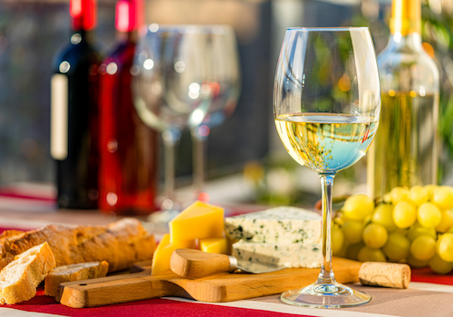 A wine and cheese setup with glasses, bottles, cheese, bread, and grapes on a table, creating a cozy and inviting atmosphere.