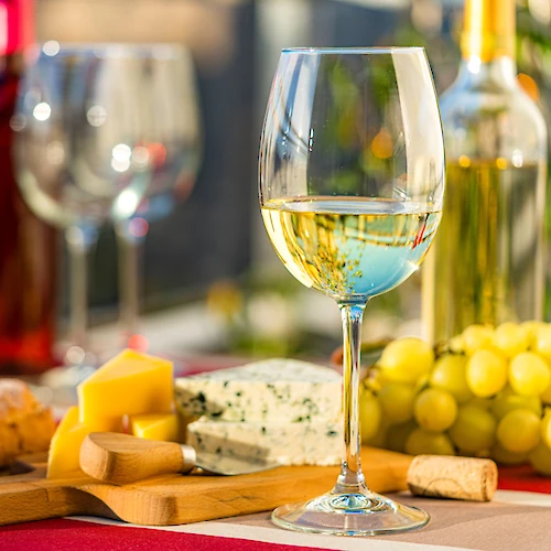 A wine and cheese setup with glasses, bottles, cheese, bread, and grapes on a table, creating a cozy and inviting atmosphere.
