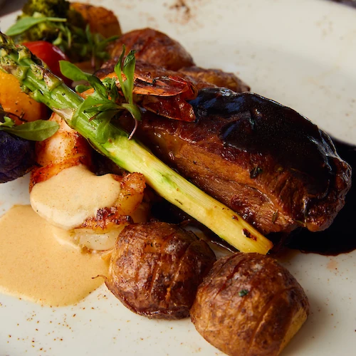 The image shows a plated gourmet dish with meat, asparagus, sauce, and roasted vegetables on a white plate.