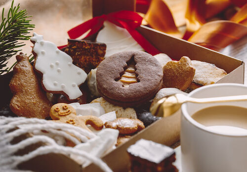 An assortment of festive cookies, including gingerbread and decorated shapes, sits beside a cup of coffee in a cozy setting.