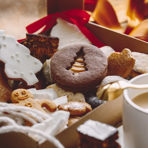 An assortment of festive cookies, including gingerbread and decorated shapes, sits beside a cup of coffee in a cozy setting.