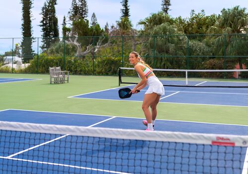 A person is playing pickleball on an outdoor court, holding a paddle and preparing to hit the ball.