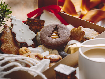 A box filled with assorted Christmas cookies, including gingerbread and frosted designs, next to a cup of tea or coffee.
