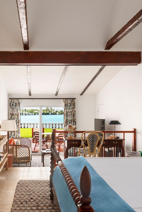 A bright hotel room with a large bed, wooden beams, and a seating area. There’s a view through the balcony doors.