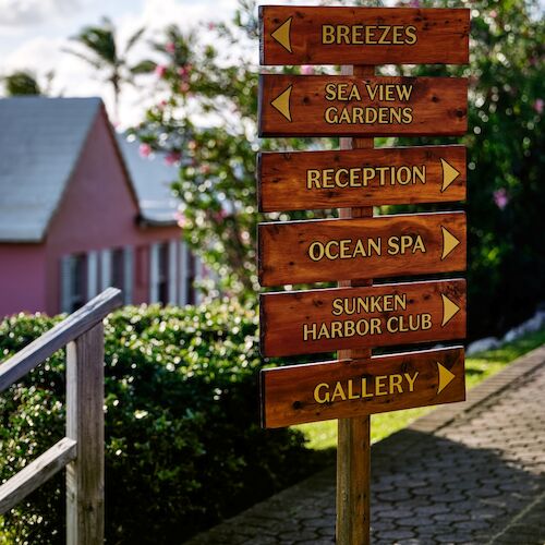 A wooden signpost displays directions to various locations, including Breezes, Sea View Gardens, and Gallery, amidst a sunny outdoor setting.