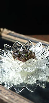 A crystal dish with a decorative item, possibly food, is placed on a reflective surface, creating an elegant display.