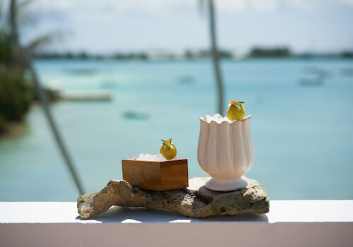 Seaside cocktails: icy pineapple-lime drinks with garnish, set on a rock by the turquoise ocean.