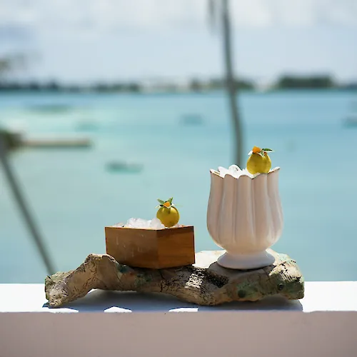 Seaside cocktails: icy pineapple-lime drinks with garnish, set on a rock by the turquoise ocean.