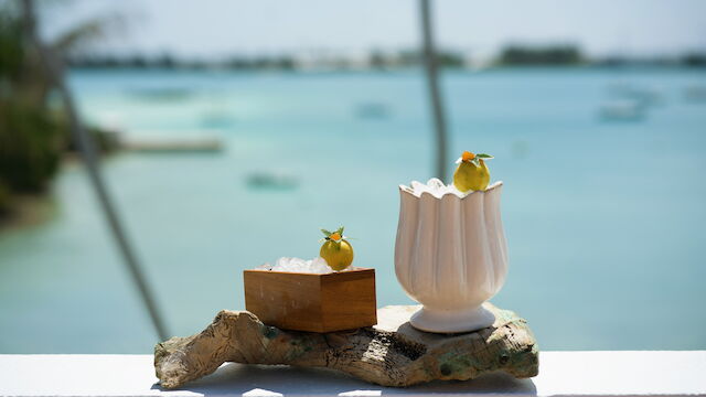 Seaside cocktails: icy pineapple-lime drinks with garnish, set on a rock by the turquoise ocean.