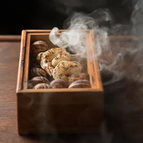 A wooden tray holds grilled chicken and seafood, steaming with fragrant smoke rising into the air.
