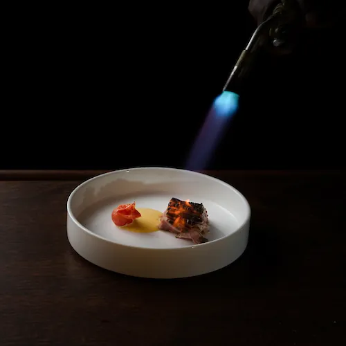 Chef torch-finishing a plated dish for the World’s Culinary Masters Series at Cambridge Beaches in Bermuda.
