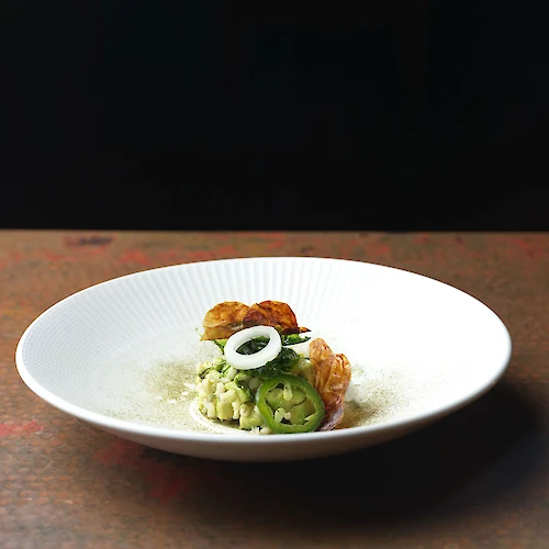 A gourmet dish featuring a carefully plated serving of risotto with prawns, garnished with a ring of onion.