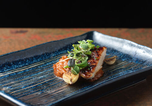 A gourmet dish is presented on a blue rectangular plate, garnished with herbs and vegetables, set against a dark background.