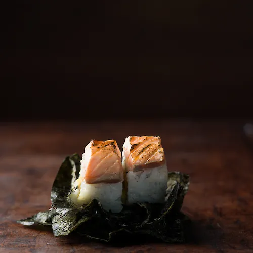 Seared fish served over dark greens with a delicate garnish, presented on a rustic wooden table