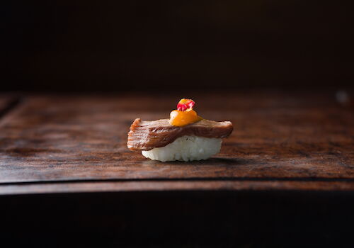 Bite-sized seafood course with a crisp golden topping and colorful garnish, presented on a dark wooden table