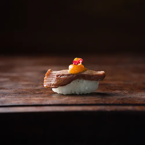 Bite-sized seafood course with a crisp golden topping and colorful garnish, presented on a dark wooden table