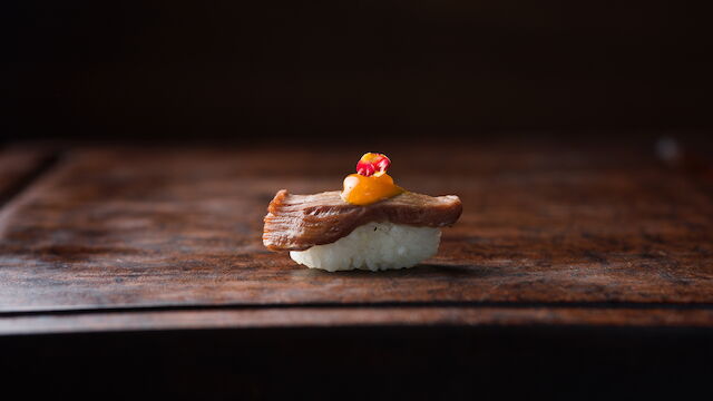 Bite-sized seafood course with a crisp golden topping and colorful garnish, presented on a dark wooden table