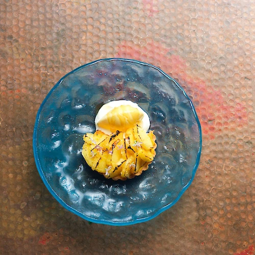 A blue plate with grilled pineapple and a scoop of ice cream sits on a textured surface.