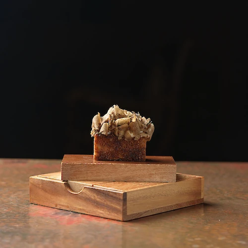 A single piece of bread with mushrooms on top is placed on a stack of wooden boxes against a dark background.
